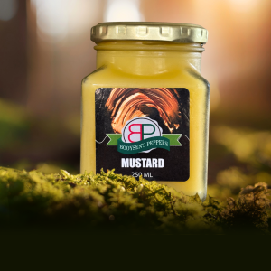 A jar of Booysens Peppers Sweet Mustard sits on green moss in a sunlit forest setting.