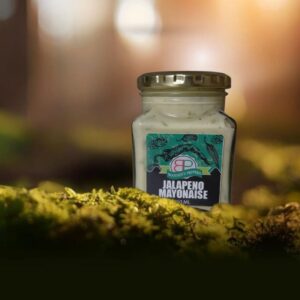 A 250 mL square glass jar of Booysen's Peppers Jalapeño Mayonnaise sits on green moss. The creamy mayonnaise is pale green with visible pepper pieces. The label is black and green with a detailed botanical pattern.
