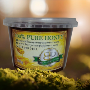 A 500g tub of Booysen's Pepper's 100% Pure Honey resting on green moss against a warm, blurred natural background. R65